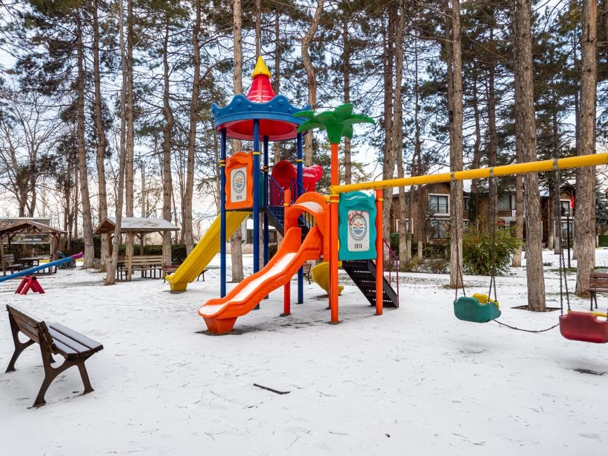 Ryškūs žaidimų aikštelės elementai snieguotame parke, primenantys saugių erdvių svarbą